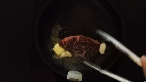 取平底鍋熱橄欖油下牛排，隨後放入大蒜、無鹽奶油跟些許迷迭香葉提香跟黑胡椒、鹽調味煎至自已喜歡的熟度後備用