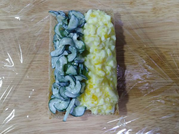 無鹽奶油均勻塗抹土司，可使土司不會太快變潮濕；再將小黃瓜、蛋沙拉鋪滿土司。土司可以依個人選擇切邊或不切。