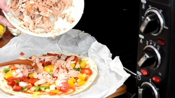 準備一片披薩皮，抹上番茄醬，撒上玉米、青椒、甜椒、洋蔥、番茄、鮭魚碎肉、小卷圈，接著鋪上起司。