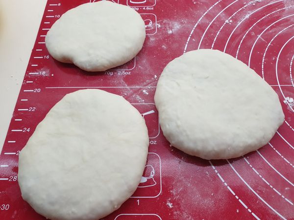 將麵糰揉一揉，平均分配大小一個一個，擀開一片，包入餡料，將收口捏緊後壓一下變扁圓型。