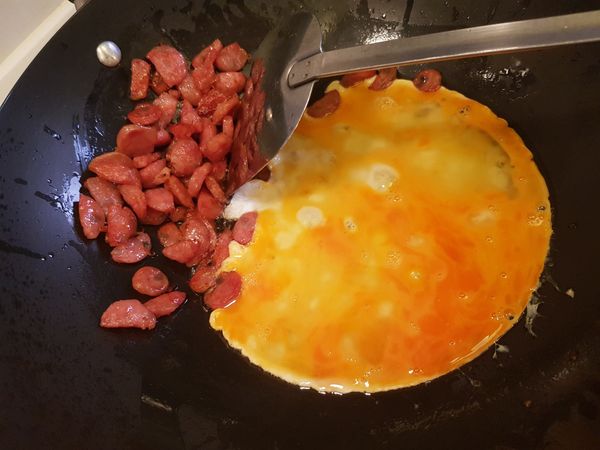 中大火熱油鍋後先將香腸煎至出油焦香微縮， 可撈出備用或是像我把香腸推在鍋子的另一邊，放入蛋液讓蛋先稍微凝固後，快速翻炒不停炒， 香腸炒煎香很重要喔， 不然吃起來就會非常油膩。