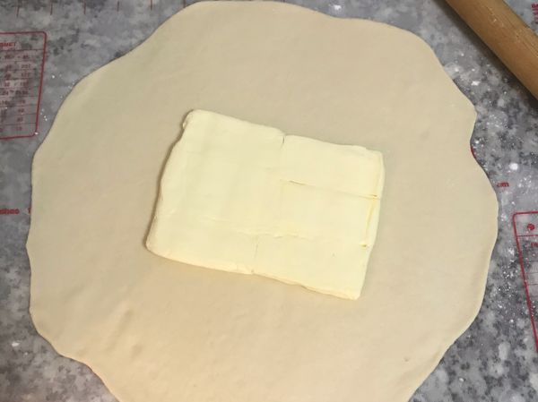 工作台上撒些手粉；將麵糰桿成圓方型；冰箱拿出奶油，除去保鮮膜，將奶油放在麵皮中間；