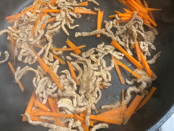 下蒜末、肉絲，炒至七分熟後，再放入紅蘿蔔略微拌炒。