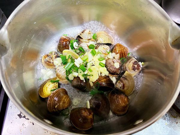 下蛤蜊，倒入蒜末、蔥花。找一個蓋子將鍋子蓋起來，悶大約1分鐘後掀蓋。