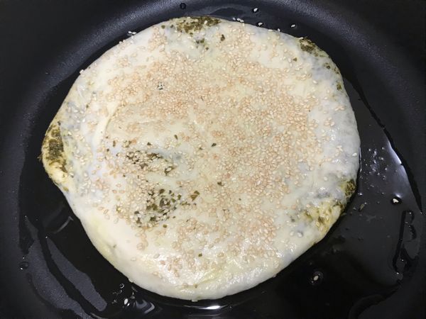 鍋子裡放油，這邊鍋子先不開火；刷ㄧ些水，灑些白芝蔴，手壓一壓，將白芝蔴壓進麵糰裡；直接在鍋裡進行二次醱酵。