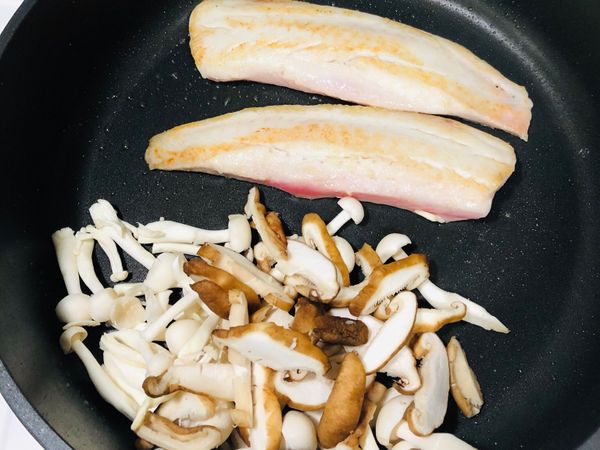 當一面變色時，輕輕用鍋鏟將魚翻面，另外把菇放入鍋中炒。