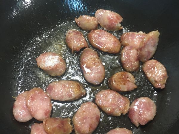 接著下香腸片炒香炒至兩面微焦黃，再加2匙醬油、白砂糖、米酒拌炒