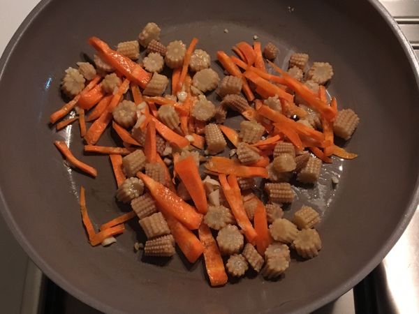 再將一些蒜頭切成小塊，先下油鍋炒香，之後將備料放入鍋中，炒紅蘿蔔、菇以及高麗菜。