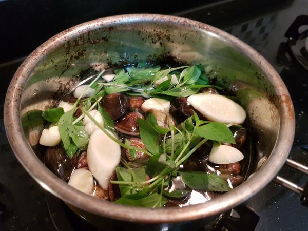 在另外一個鍋子放入蛤蜊、大蒜、薑片、九層塔，並倒入米酒和雞高湯，將蛤蜊煮熟撈起，並將辛香料的味道煮進湯裡。