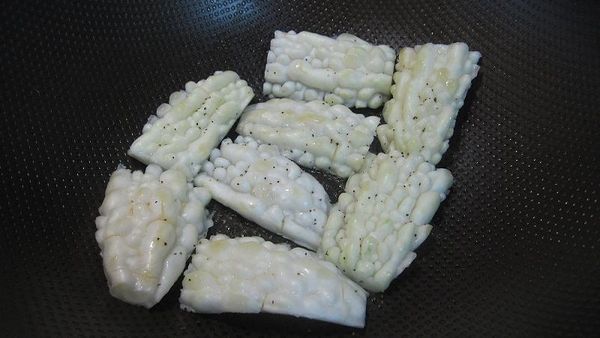 放入鍋內並灑上少許黑胡椒粒把2面都煎成金黃色（各約3分鐘）。《可加蓋燜煎，可加速煎黃的時間，若個人不喜歡油煎的方式，也可用水煮法，把苦瓜燙軟也行》