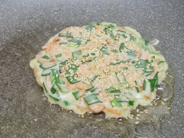 熱油鍋放入麵糊，麵糊鋪平後上面撒滿白芝麻，中火慢煎。