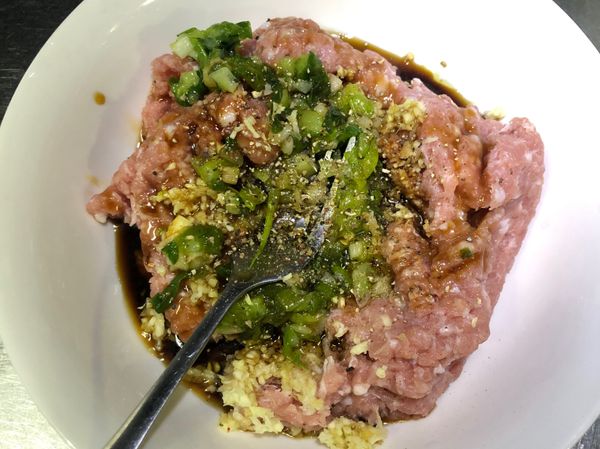 將蔥薑蒜放入絞肉中，加入調味料一起抓醃，摔打至醬汁都吃入絞肉中，且更有黏性的肉團。