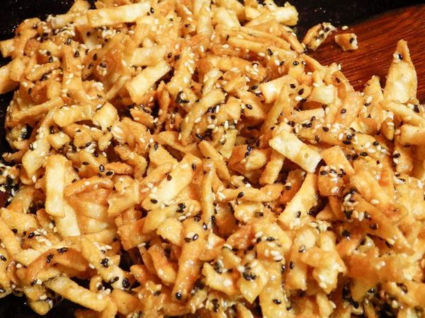 糖溫煮到110度時，（用木匙撈起糖漿流動時最後會有牽絲的狀態出現）把炸好的餃子皮，芝麻全放入鍋裡用木匙開始攪拌幾下，此時可關火了…
（材料若事先放入烤箱裡保溫，糖溫則煮到115度時立即關火，若沒有則是照上述的食材放入攪拌一下再關火。）