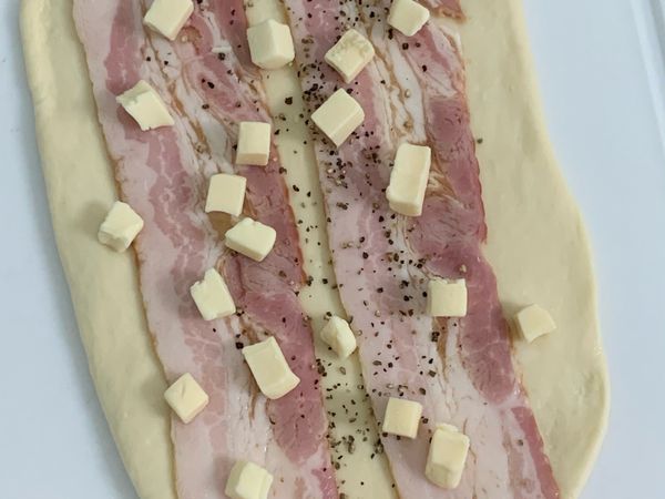 攪拌完取出將麵團對半，桿成長型，加入培根、高熔點乳酪丁，可以灑點黑胡椒粉，捲起整型放回