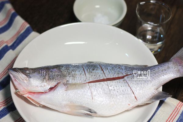 超市買回來的鱸魚都已經處理過了，所以只要將魚洗淨後，廚房紙吸乾水份，拿刀子在魚身二側，斜切3~4刀。
使用米酒和鹽，將魚醃個10分鐘(中間要不時翻面，讓魚身二側都有均勻醃到)。
魚醃好時，可用廚房紙巾略為擦乾。
