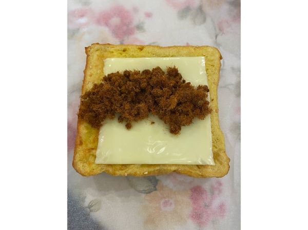 起鍋後，準備一張烘焙紙或鋁箔紙，將吐司放在上面，再放上一片起司和肉鬆即可捲起