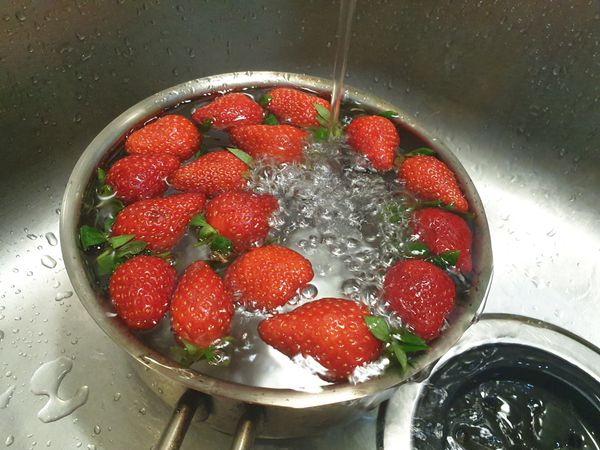 這時候可以洗草莓，先用水一直清洗，用手稍微攪動清洗，但要溫柔，不要把草莓戳破皮啦！最後再用過濾水清洗，泡個3分鐘。然後把草莓蒂頭去除，草莓再切半。