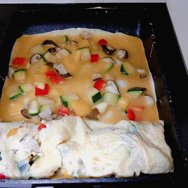 取厚蛋燒鍋抹上少許沙拉油，將拌好材料的蛋汁取一湯勺放入鍋底（開小火），用筷子輕輕撥動讓蛋液收乾凝固，捲起成長條狀，再次在鍋底抹上少許沙拉油，再淋上一勺蛋液，一樣輕輕擀捲起，再由上面和側邊緊壓，讓煎好的厚蛋燒更緊密紮實。