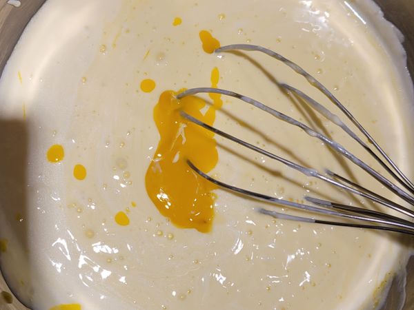 在已融合的奶油乳酪糊中，加入蛋黃，香草精跟檸檬汁拌勻。