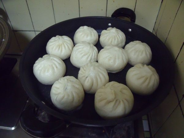 鍋裡放一大匙的油,放入包子,用小火煎,煎至底部有焦黃,再放入半杯的水,蓋上鍋蓋。