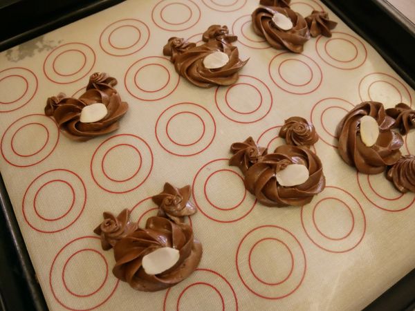 在烤盤上先擠出一個大圓形（臉）、再擠兩個小圓形（耳朵）臉上放一片杏仁片後放入預熱170度烤箱約8-10分鐘。取出放涼後再以巧克力裝飾眼睛及鼻子。