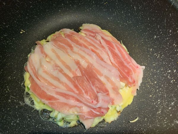 平底鍋加油，開中小火，倒入一半麵糊，鋪上豬五花肉片，鍋蓋蓋上悶煎約3分鐘。
翻面，蓋鍋蓋再悶煎約3分鐘。
（可用筷子稍微戳麵糊，確認是否煎熟）