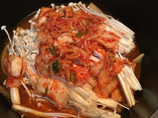 放入金針菇及1/2碗泡菜。水不用加多，因為金針菇會出水。蓋上鍋蓋小火煮約10分鐘，讓油豆腐入味。