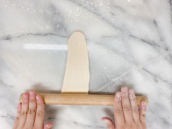 用擀麵棍將麵糰壓延成約25cm~30 cm的長度。

註1：如果家裡的平底鍋沒有那麼大，也可以將麵糰滖圓後擀成大小適當的圓形薄餅。
註2：擀開後若麵團太緊回縮太多，可暫放旁邊先擀下一片後再回頭桿長即可。