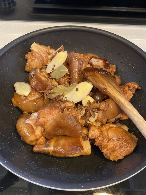 把豬腳倒回鍋中，仔細拌炒讓糖色上均勻，接著放入薑片、蔥段、八角、花椒粒。