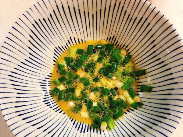 將雞蛋打入蔥花中，加入的1/2湯匙醬油露後；進行打蛋的動作。