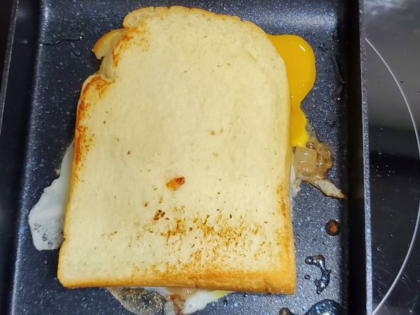將吐司直接覆蓋在尚未全熟的煎蛋上，靜待1分鐘，使蛋液熟透並與吐司貼合後，進行修邊。