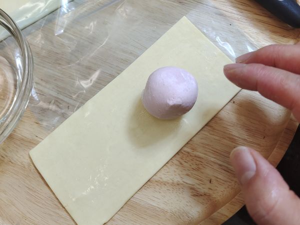 記得準備一些冷水或冷開水備用。
把冷凍的湯圓及稍微退冰的酥皮(不要退冰太久、大概讓冷凍餅皮可以折彎的程度就好)、其中一邊放上草莓煉乳湯圓、然後其他的面積就塗滿了冷水或冷開水、小心的把酥皮對折、湯圓包在裡面折好。