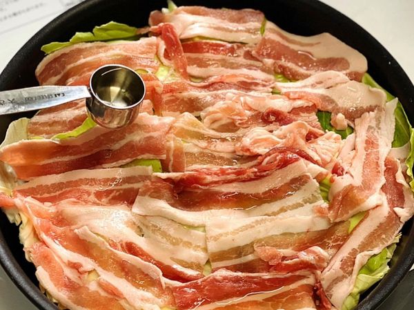 把高麗菜鋪在煎鍋上，把豬肉放在不重疊的地方。然後撒上鹽和料理酒。