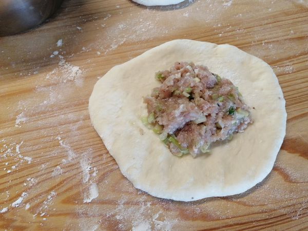 將麵糰擀成薄圓麵皮，放上適量的肉餡。
