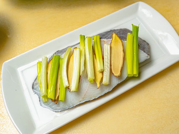 將鱈魚洗淨後擦乾，放上薑片及蔥，淋上米酒。