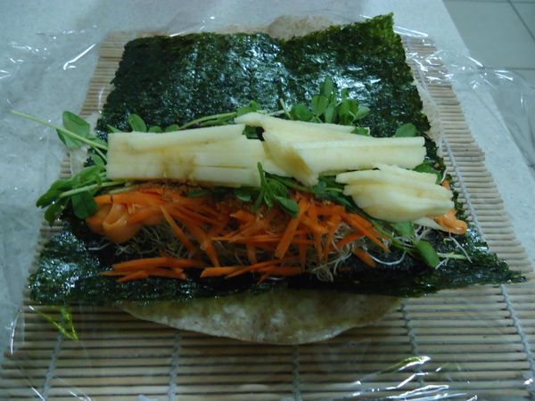 白色的是蘋果。鋪上海苔片是為了吸溼，也增添營養與口感。全麥餅皮→海苔片→黑芝麻粉→苜宿芽→沙拉醬→素香鬆→豌豆苗→紅蘿蔔絲→葡萄乾→蘋果條→捲起來即可。