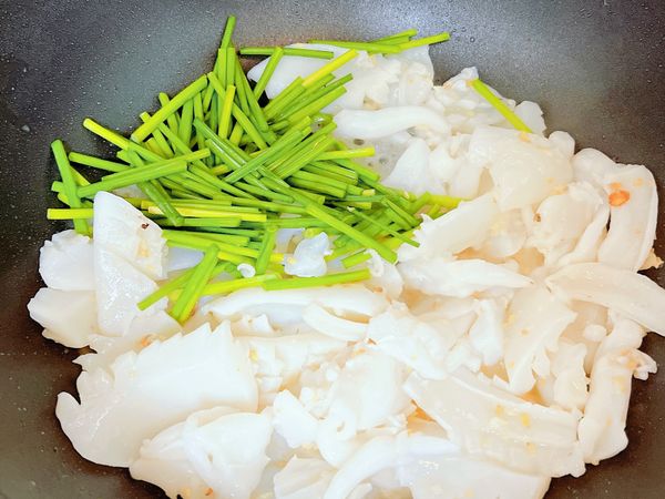 炒到花枝稍微捲曲時，先將韭菜花頭入鍋一起翻炒。