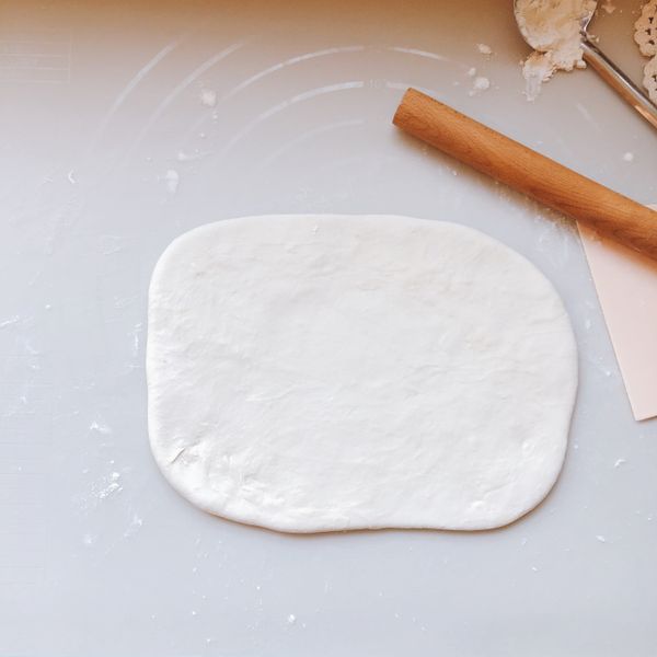 案台灑粉，將麵團擀成矩形。