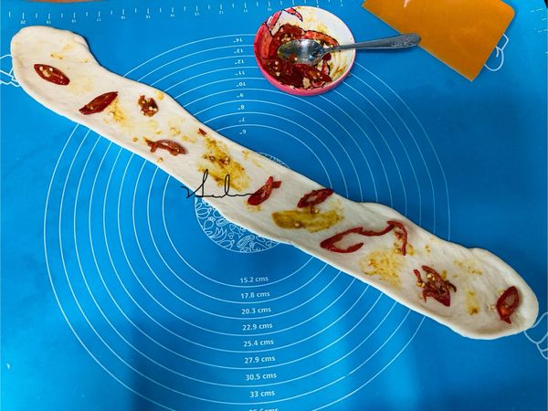 將第2個小麵糰壓平，桿成長條狀，放入剛拌好的咖哩辣椒醬，先放辣椒，要左、右有間隔的放置，不可以一坨或一堆的放，免得捲時會爆開，放完辣椒後用小湯匙背面將咖哩醬交叉塗在空白處，並將麵糰捲起，放在一邊。咖哩辣椒口味。