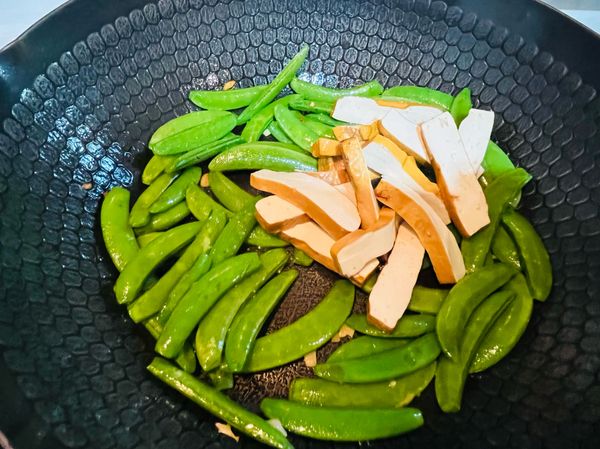 炒到甜豆表面呈現油綠色，即可倒入豆干拌炒，再加入適量的鹽調味，快炒幾下，即可盛盤上桌