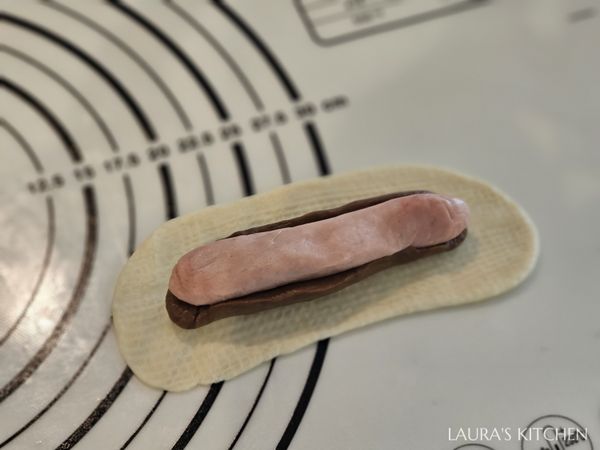 把可可麵團微微擀平(約12公分)，把粉紅色麵團放在中間，用可可麵團包覆住兩側、但不用完全包住。再放到擀開的白色麵團上，把粉紅可可麵團整個包進去裡面，收口捏緊。