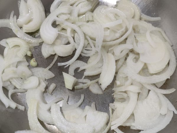 加熱平底鍋，倒入食用油，洋蔥切頭尾，去老皮，切成絲，放入鍋中爆香拌炒。