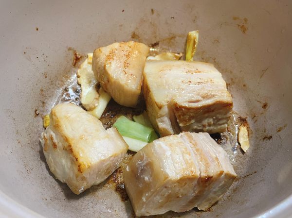 起薄油鍋，將蔥白、薑片、五花肉煸到略焦黃