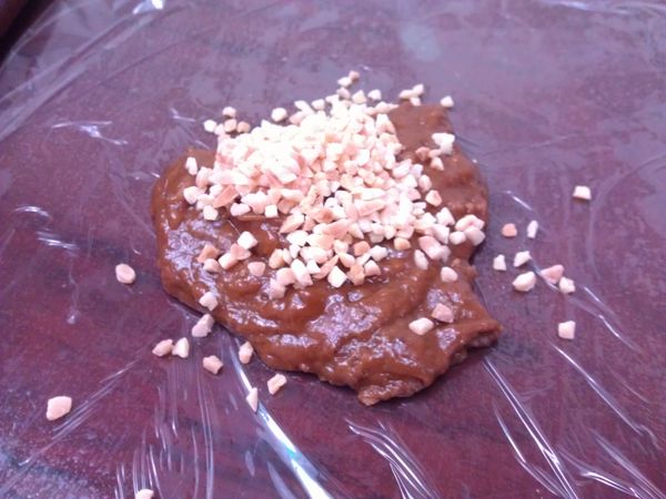 預熱烤箱至攝氏160度。工作檯舖上保鮮膜，放上一半的餅乾麵糰，加入熟杏仁角，折起一半的保鮮膜蓋上，隔著保鮮膜將麵糰與杏仁角按壓混合均勻。