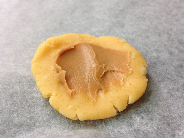 拌好的麵糰，取約12公克左右，搓揉成球狀後壓扁，中間抹上適量的花生醬如圖。