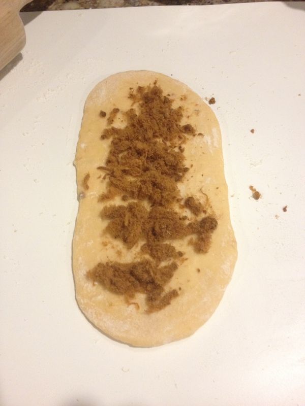 休息好的麵團表面灑些中筋麵粉，橄成長形後翻面，再鋪上肉鬆捲起