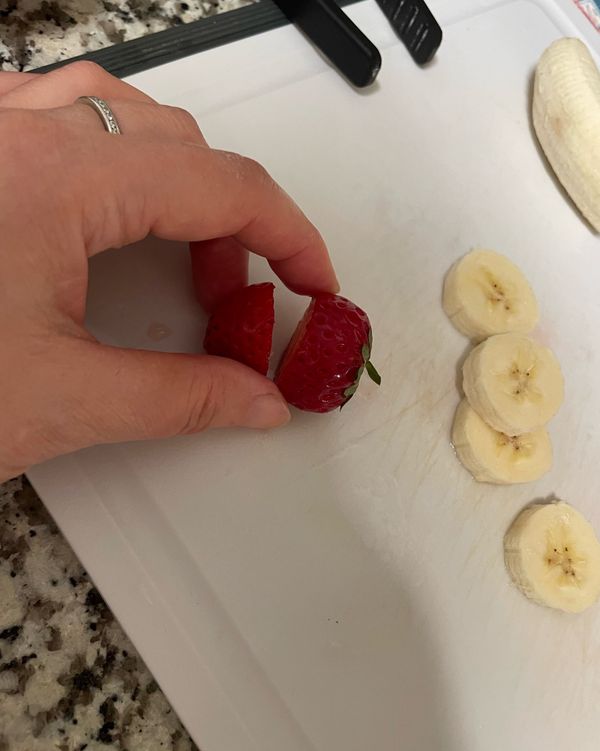 將草莓洗乾淨之後，從三分之二的地方解開，尖尖的地方當成帽子，綠色的蒂當成身體的領子，香蕉切片，拿牙籤串起來，香蕉上面放上兩顆黑芝麻當眼睛