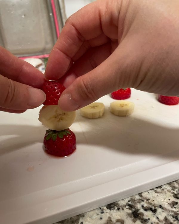 將草莓洗乾淨之後，從三分之二的地方解開，尖尖的地方當成帽子，綠色的蒂當成身體的領子，香蕉切片，拿牙籤串起來，香蕉上面放上兩顆黑芝麻當眼睛