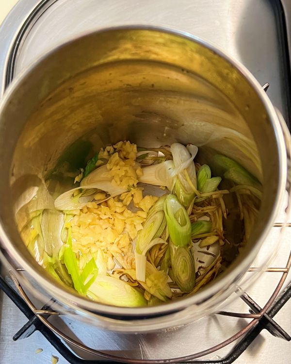 內鍋放入香油，小火加熱，放入薑絲、蒜苗白炒香。再加入酸菜炒香。