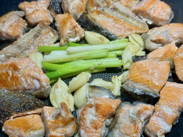 ●用料理長筷幫鮭魚一一翻面，再補剩下1大匙油進鍋中，把蒜瓣跟蔥白段加進來一起煎香。

※鮭魚尾段油脂少皮多，若用鮭魚腹部部位油脂多，這裡就可以不用再加油。